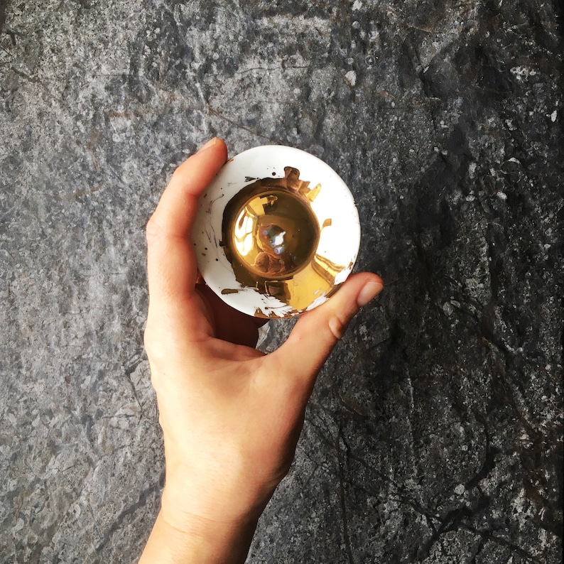 K&ouml;nnte beinhalten: Eine kleine, wei&szlig;e Keramikschale mit goldenem Innenraum. Die Schale hat einen leicht erh&ouml;hten Rand und eine glatte, gl&auml;nzende Oberfl&auml;che.