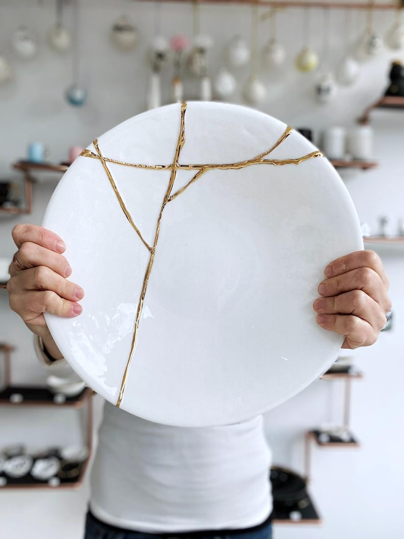 A large white circular platter with gold cracks. The plate is made of ceramic and has a smooth, glossy finish.