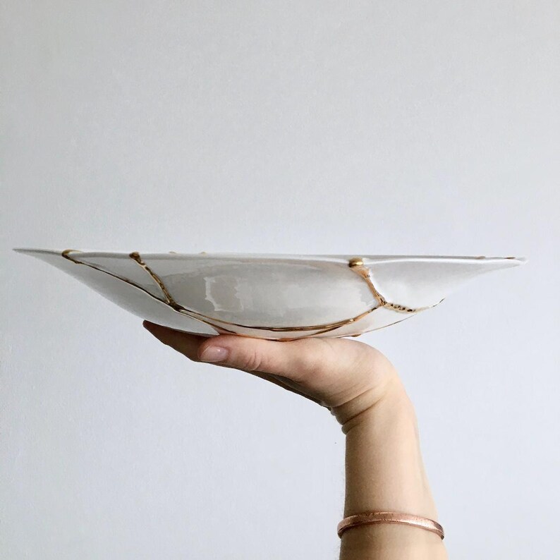 A large white circular platter with gold cracks. The plate is made of ceramic and has a smooth, glossy finish.