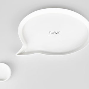 May include: White ceramic serving dish shaped like a speech bubble with the word "YUMMY!" written inside. The dish is on a white background.