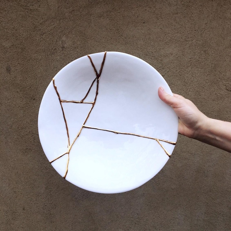 A large white circular platter with gold cracks. The plate is made of ceramic and has a smooth, glossy finish.