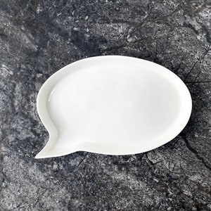 May include: White ceramic serving dish shaped like a speech bubble. The dish is empty and has a smooth, glossy finish.