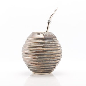 May include: A brown ceramic mate gourd with a silver bombilla straw. The gourd has a textured, ribbed design.