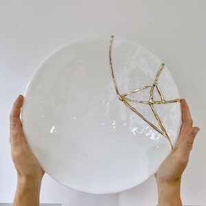 A large white circular platter with gold cracks. The plate is made of ceramic and has a smooth, glossy finish.