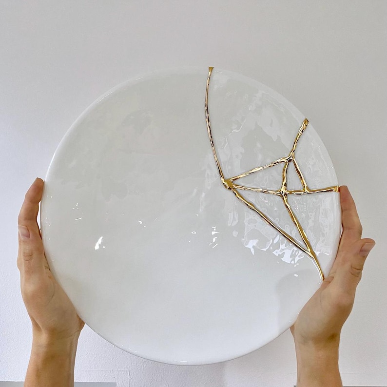 A large white circular platter with gold cracks. The plate is made of ceramic and has a smooth, glossy finish.