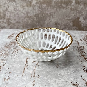 May include: White ceramic bowl with a gold rim and a delicate, openwork design. The bowl is perfect for serving small snacks or holding jewelry.
