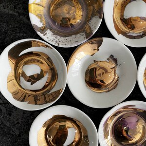 K&ouml;nnte beinhalten: Set aus sieben wei&szlig;en Keramikschalen mit goldenen Akzenten. Die Schalen haben ein einzigartiges, abstraktes Design mit goldener Farbe, die auf die Oberfl&auml;che gespritzt wurde. Die Schalen sind perfekt zum Servieren von Snacks, Dips oder Desserts.