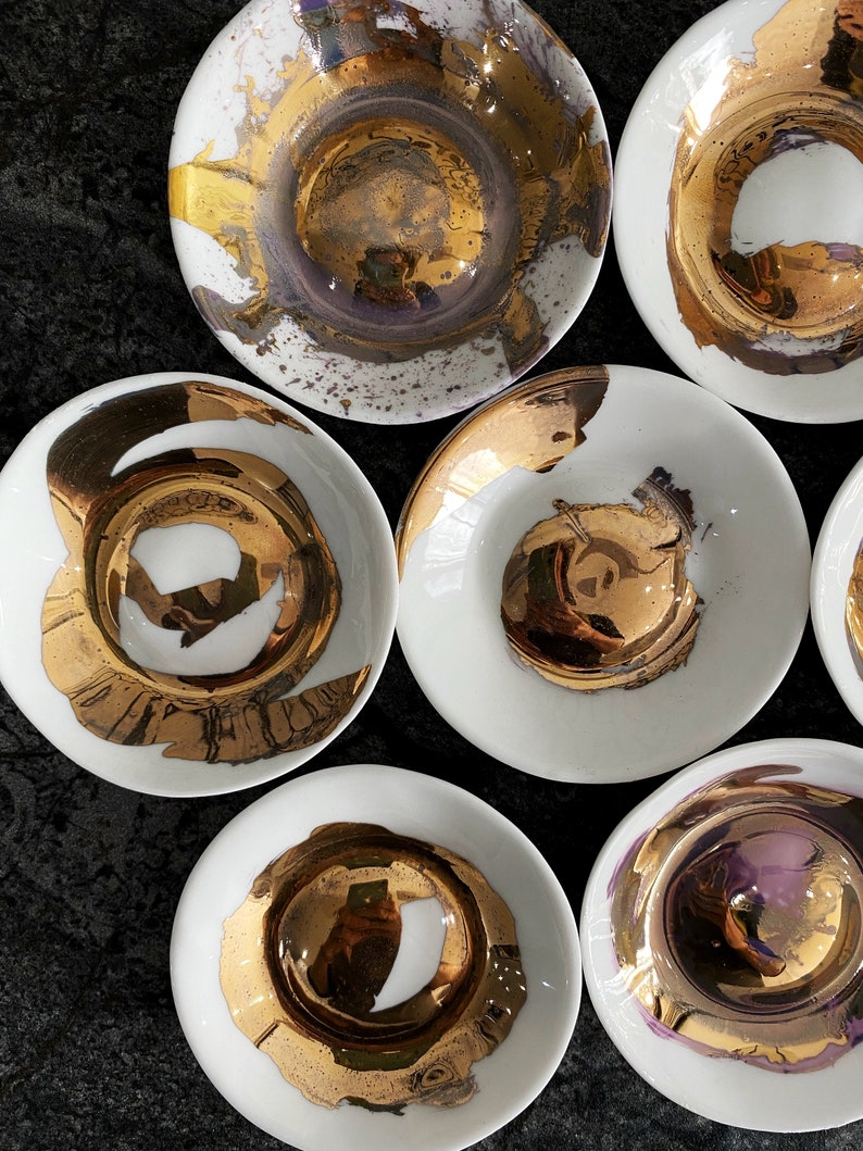 K&ouml;nnte beinhalten: Set aus sieben wei&szlig;en Keramikschalen mit goldenen Akzenten. Die Schalen haben ein einzigartiges, abstraktes Design mit goldener Farbe, die auf die Oberfl&auml;che gespritzt wurde. Die Schalen sind perfekt zum Servieren von Snacks, Dips oder Desserts.