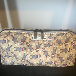 May include: A rectangular beige zipped bag featuring a repeating pattern of sock monkey figures wearing red and white striped hats. The bag has a grey zip and grey end panels. The word "Wont" is visible on a small tag.
