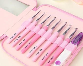 May include: A set of eight crochet hooks with pink handles and silver metal tips, organized in a pink zippered case. The hooks are labeled with sizes 4/0 2.5mm, 5/0 3.0mm, 6/0 3.5mm, 7/0 4.0mm, 7.5/0 4.5mm, 8/0 5.0mm, 9/0 5.5mm, and 10/0 6.0mm.