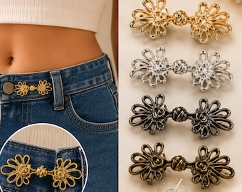 May include: A set of four metal clothing fasteners in gold, silver, black, and bronze tones. Each fastener features a symmetrical, open-work floral design with a central knot detail. One fastener is shown attached to the waistband of blue jeans.