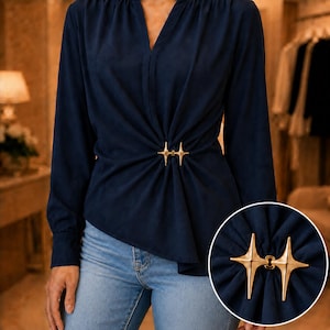May include: A long-sleeved navy blue blouse featuring a V-neckline and a gathered waist detail secured by a gold-toned, star-shaped metal clasp. The fabric drapes from the centre point, creating soft folds across the front of the garment.