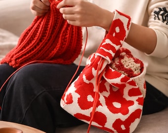 May include: A red and white patterned tote bag with a matching handle. The bag is made of a knitted material. A person is knitting a red hat with wooden needles. The hat is in the process of being made.