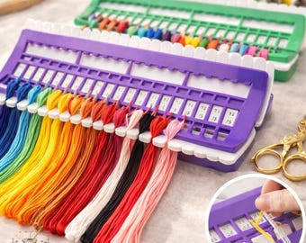 May include: A close-up of two thread organizers filled with colorful embroidery floss. The front organizer is purple with white accents and holds a rainbow of threads. The second organizer is green. Gold scissors are in the background.