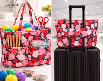 May include: A floral print craft tote bag with multiple pockets, filled with yarn, crochet hooks, and scissors. The bag is placed on top of a black suitcase. The tote features a red, pink, and white rose pattern.