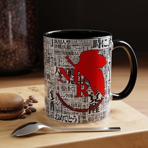 May include: Black and white ceramic mug with a black handle and interior. The mug features Japanese text and a red graphic. A spoon, coffee beans, and a pastry are on a wooden surface.
