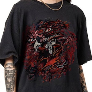 May include: Dark gray t-shirt featuring a detailed red and black graphic of a character holding a gun, surrounded by demonic imagery and multiple eyes. The design is centered on the shirt.