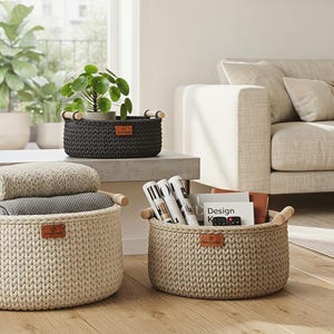 May include: A set of four round storage baskets made of thick, braided rope in olive green, dark grey, cream, and beige. Each basket features two light-coloured wooden handles on the sides and a small rectangular brown leather-like brand tag on the front.