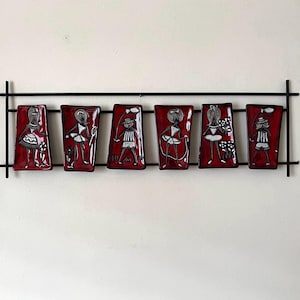 May include: A wall-mounted artwork comprising six red rectangular tiles, each with a black and white figure, set within a black metal frame. The figures on the tiles appear to be engaged in various activities, creating a playful theme.