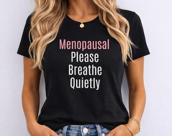 May include: A black short-sleeved t-shirt featuring the text Menopausal in pink lettering, followed by the words Please, Breathe, and Quietly in white lettering centered on the chest. The shirt has a crew neckline and a standard fit design.