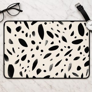 May include: A rectangular laptop skin featuring a cream-colored background with a scattered pattern of black, organic, leaf-like shapes and small dots. Some of the black shapes have a textured, spray-painted effect along their edges.