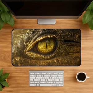 Puede incluir: Una alfombrilla de escritorio rectangular con un gráfico de alta resolución en primer plano de un ojo de reptil. La imagen muestra un iris amarillo dorado vibrante con una pupila negra vertical, rodeado de texturas de piel escamosa marrón.