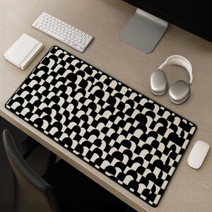 May include: A rectangular desk mat featuring a repeating geometric pattern of black and cream-coloured semicircles and squares. The mat has a clean, flat surface with a black border, designed to sit on a desk beneath a keyboard and mouse.