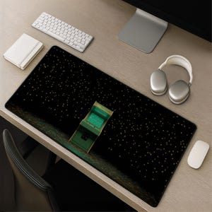 May include: A rectangular desk mat featuring a black background with a scattered pattern of small yellow stars and a single green arcade cabinet graphic positioned in the center. The mat has a smooth surface and black stitched edges for durability.