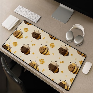 May include: A rectangular desk mat featuring a repeating pattern of cartoon bees with brown and yellow stripes, small wings, and tan berets, interspersed with yellow honeycomb shapes on a light cream-colored background with a black border.