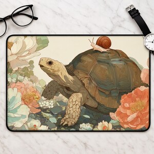Peut inclure: Un tapis de bureau rectangulaire illustrant une grande tortue brune avec un petit escargot sur sa carapace, entourée de grandes fleurs aux tons doux pêche, blanc et crème. L'illustration présente un aspect texturé et pictural.