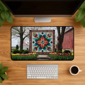 May include: A desk mat with a vibrant quilt design. The quilt showcases a central star motif in red, teal, and cream, framed by a border. The background depicts a rural landscape with trees, a red barn, and a flower bed, creating a rustic feel.