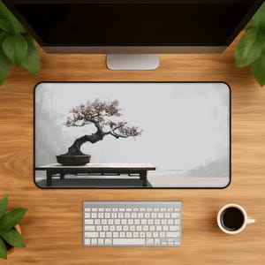 May include: A rectangular desk mat featuring a printed illustration of a dark, gnarled bonsai tree in a ceramic pot resting on a low wooden table against a soft, light gray background. The mat has a black border and a smooth, flat surface.