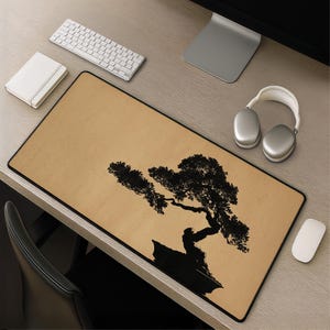 May include: A rectangular desk mat featuring a tan, textured background with a black silhouette of a bonsai tree in a pot. The mat has a thin black border and is positioned on a desk surface alongside a white keyboard, mouse, and headphones.