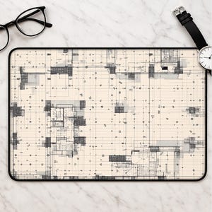 May include: A rectangular desk mat featuring a cream-coloured background with a detailed black architectural floor plan grid. The mat has a thin black border and is positioned near a pair of black-rimmed spectacles and a black wristwatch.