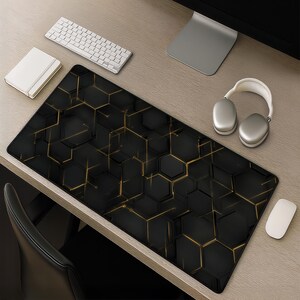 Könnte beinhalten: Eine rechteckige Schreibtischunterlage mit einem schwarz-goldenen geometrischen Muster aus ineinandergreifenden Sechsecken und dünnen, leuchtend goldenen Linien, die die Formen verbinden. Die Unterlage liegt auf einer Holzoberfläche neben Tastatur, Maus und Kopfhörern.