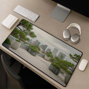 Peut inclure: Un tapis de bureau rectangulaire présentant une impression photographique haute résolution d'une terrasse sur le toit avec plusieurs arbres et arbustes à feuillage persistant en pot. L'arrière-plan montre un paysage urbain.