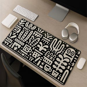 May include: A rectangular desk mat featuring a black and white graphic pattern of stylized potted plants, cacti, and abstract shapes. The design includes repeating geometric motifs, small stars, and a central character with a simple face.