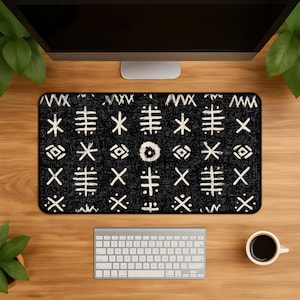 May include: A black desk mat featuring a white tribal design. The mat is on a wooden desk, with a computer monitor, keyboard, and a coffee cup. The mat's dimensions are not visible.