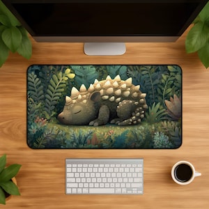 May include: A rectangular desk mat featuring a sleeping ankylosaurus dinosaur with light-coloured spikes on its back, surrounded by a dense, dark green forest of ferns and foliage. The illustration uses a palette of deep greens and earthy tones.