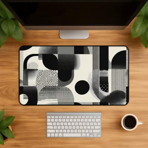 May include: A rectangular desk mat featuring a black, white, and grey abstract geometric pattern. The design includes various shapes such as circles, semicircles, and rectangles, combined with textures like vertical lines, dots, and gradients.