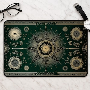 Könnte beinhalten: Eine rechteckige Schreibtischunterlage mit dunkelgrünem Hintergrund und komplizierten goldenen Himmelsillustrationen. Das Design umfasst einen zentralen Stern, mehrere Sonnenmotive und verschiedene planetare Symbole in symmetrischer Anordnung.