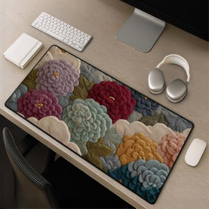 May include: A rectangular desk mat featuring a dense, textured floral pattern with large, rounded blossoms in shades of lavender, deep red, teal, mustard yellow, and soft pink, accented by muted green leaves and cream-colored cloud-like shapes.