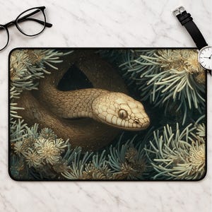 May include: A rectangular desk mat featuring a detailed illustration of a tan snake coiled among pale green pine needles. The snake has visible scales and a focused gaze, surrounded by textured foliage in shades of muted green and cream.
