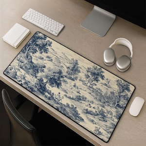 May include: A rectangular desk mat featuring a detailed blue and cream toile de jouy pattern. The design depicts a pastoral landscape with rolling hills, scattered trees, small figures, and animals, all rendered in a classic monochromatic style.