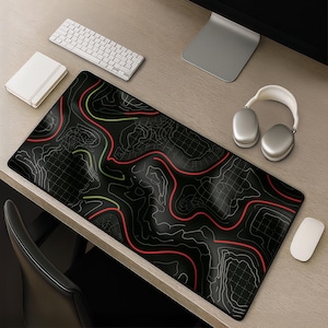 Può includere: Un tappetino da scrivania rettangolare con sfondo nero e un design a mappa topografica composto da linee bianche, rosse e verde chiaro. Il motivo presenta curve di livello fluide e sezioni a griglia distribuite su tutta la superficie.