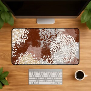 May include: A rectangular desk mat featuring a deep rust-brown background with a repeating pattern of large, intricate white and beige floral mandala-style motifs. The design has a textured, painterly appearance with soft edges and varied color tones.