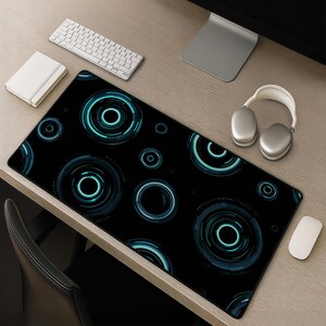 May include: A rectangular desk mat featuring a black background with a repeating pattern of glowing cyan blue concentric circles and digital ring motifs. The mat has a smooth surface and is positioned on a wooden desk surface with computer accessories.