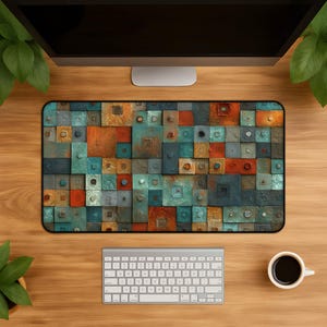 Può includere: Un tappetino da scrivania rettangolare con un motivo a mosaico di blocchi quadrati e rettangolari nei toni del verde acqua, arancione ruggine, rame e blu scuro. La superficie ha un aspetto strutturato e usurato con piccoli dettagli circolari.