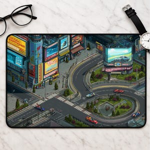 May include: A rectangular desk mat featuring a detailed isometric pixel art cityscape with multi-story buildings, illuminated billboards, and a winding road with small racing cars. The scene includes a central roundabout with green landscaping.