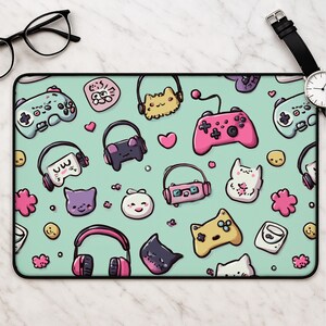 May include: A rectangular desk mat featuring a light mint green background with a repeating pattern of colorful gaming controllers, headphones, small cat faces, and pink hearts. The design includes various cartoon-style elements in shades of pink, yellow, white, and purple, creating a dense, playful graphic print across the entire surface of the mat.